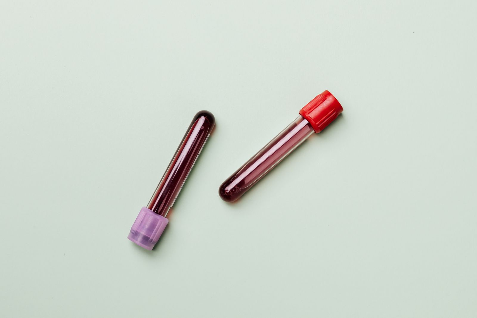 Two blood sample tubes on a pale green surface